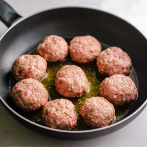 Raw, uncooked meatballs arranged in a frying pan with a small amount of oil, ready to be cooked.