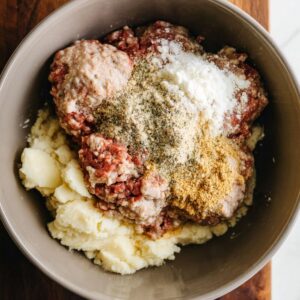 A mixing bowl containing ground meat combined with seasonings and other ingredients, ready to be shaped into meatballs.