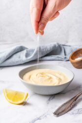 Sprinkling salt into a bowl of creamy Dijonnaise sauce.