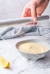Covering a bowl of dijonnaise with plastic wrap before refrigerating.