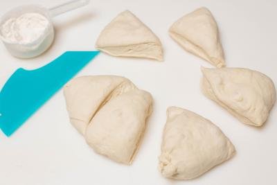 Dough being separated into equal pieces on a floured cutting board