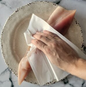 hand with a paper towel patting a piece of raw tuna loin down