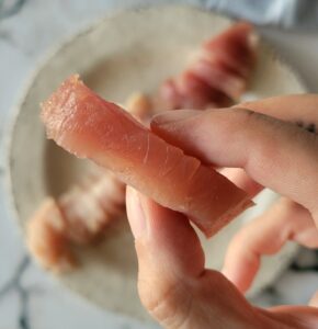 hand holding a slice of raw tuna over a plate with more