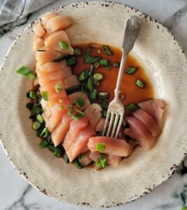 plate of sliced tuna with green onions and soy sauce, fork on the plate