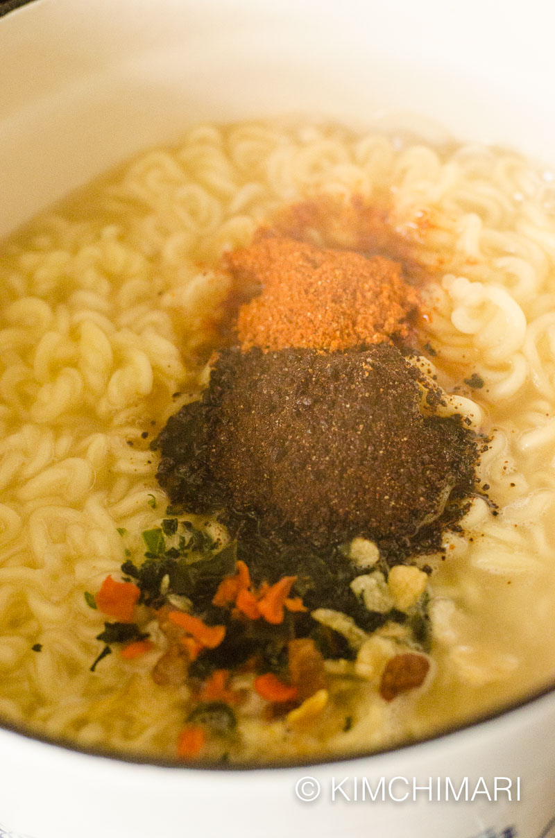noodles boiling in pot with soup and dry flakes packets all added