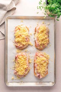 Four slices of bread topped with ham, cheese, and onions are arranged on a baking sheet, ready to become a delicious croque monsieur. A towel and a green potted plant sit nearby.