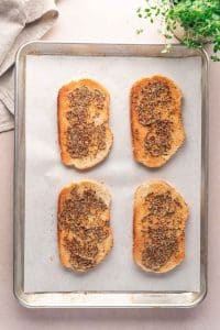 A baking sheet with four slices of toasted bread topped with a croque monsieur-inspired seasoning mixture, placed on parchment paper.