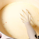 yogurt stew in a pink dutch oven, with a whisk inside