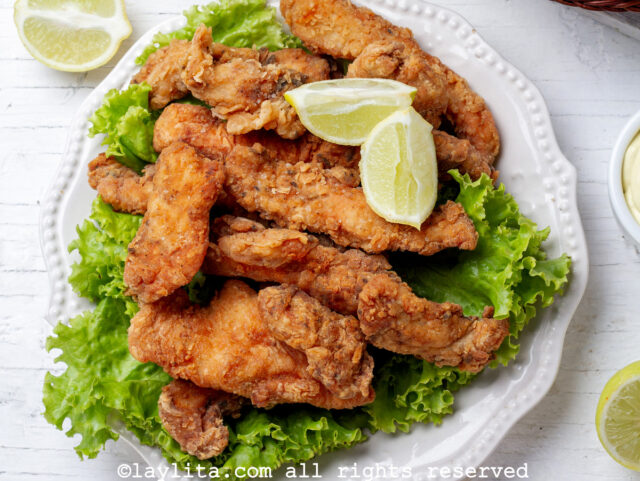 Overhead shot of chicharron de pollo on a plate lined with a bed of lettuce, garnished with limes.