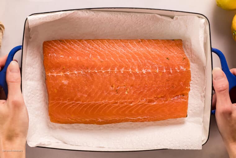 Overhead photo of two hands moving a cured piece of salmon that