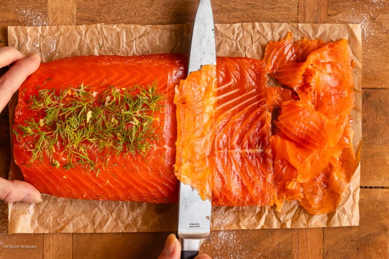 Overhead action photo of a sharp slicer cutting cured salmon gravlax into thin pieces.