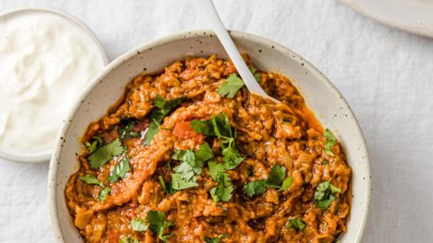 Baingan Bharta garnished with cilantro in a bowl with a white spoon served with yogurt and naan