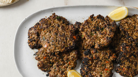 Chapli Kabab on a platter with naan, rice, salad, and raita on the side.
