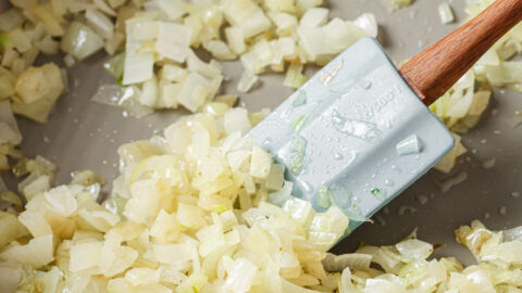 Sautéed onions in a skillet with a rubber spatula.