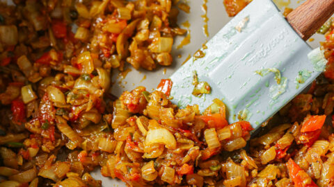 Sautéed onions, garlic, green chili, spices and tomato in a skillet with a rubber spatula.