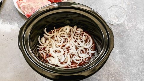 a crockpot with thinly sliced onions on the bottom